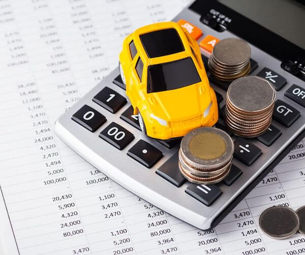 a toy car on a calculator with coins beside it buying or leasing your vehicle